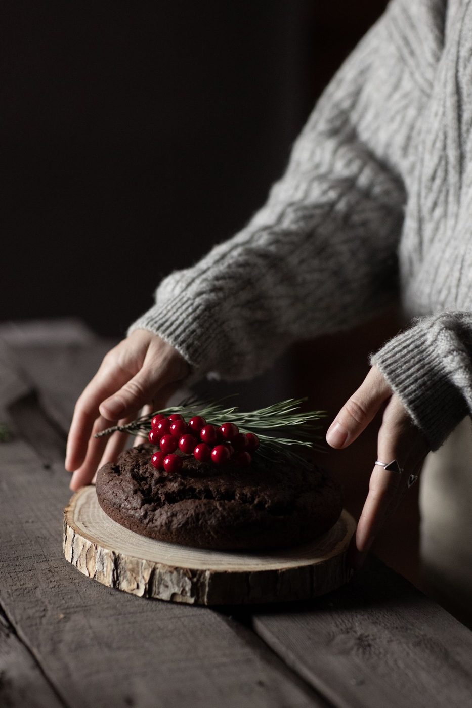 木の台に載せたチョコレートのホールケーキに、赤い実と松の葉を飾りつけているところ