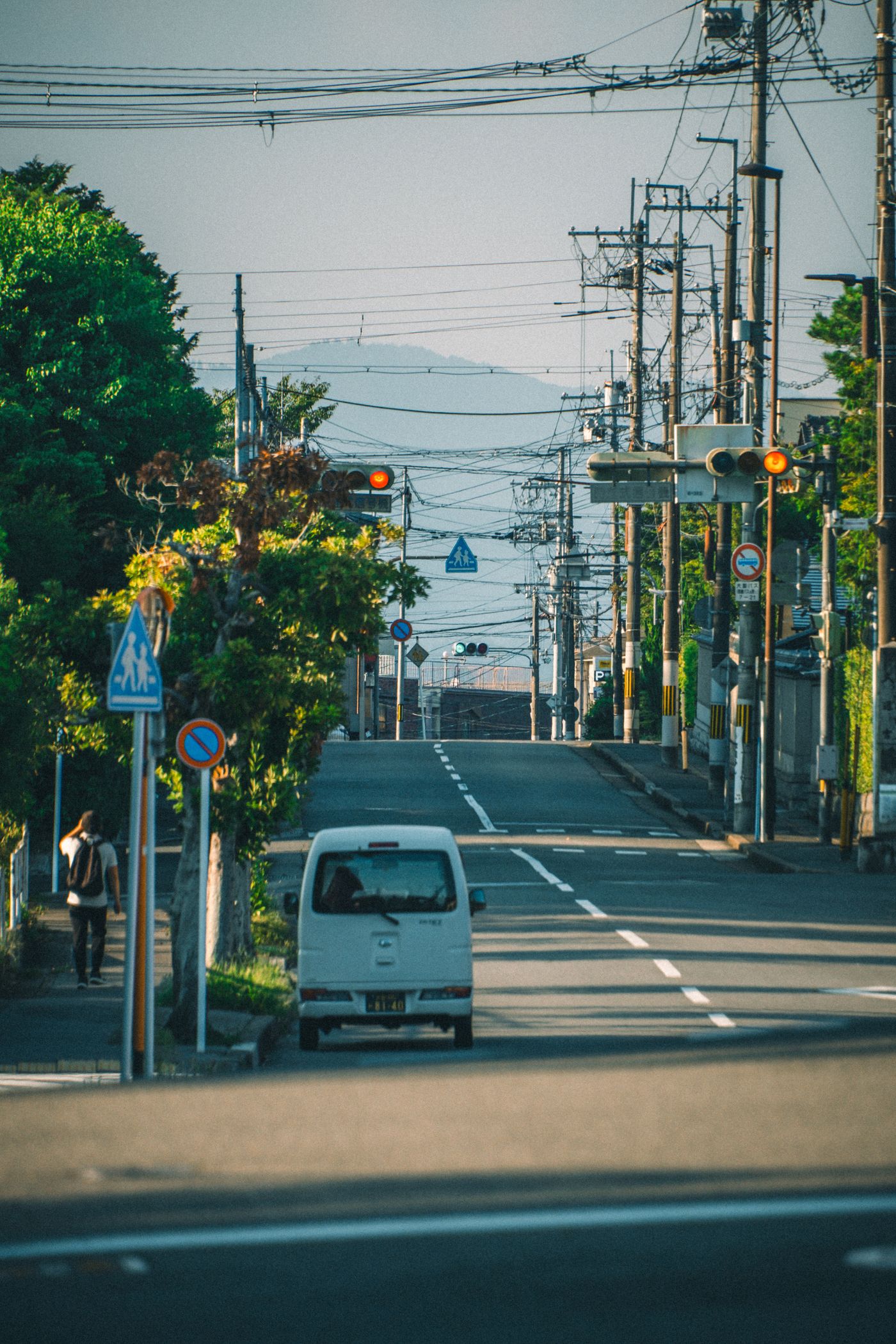 送迎エリアの住宅街を走る軽自動車と、その先に見える山並み