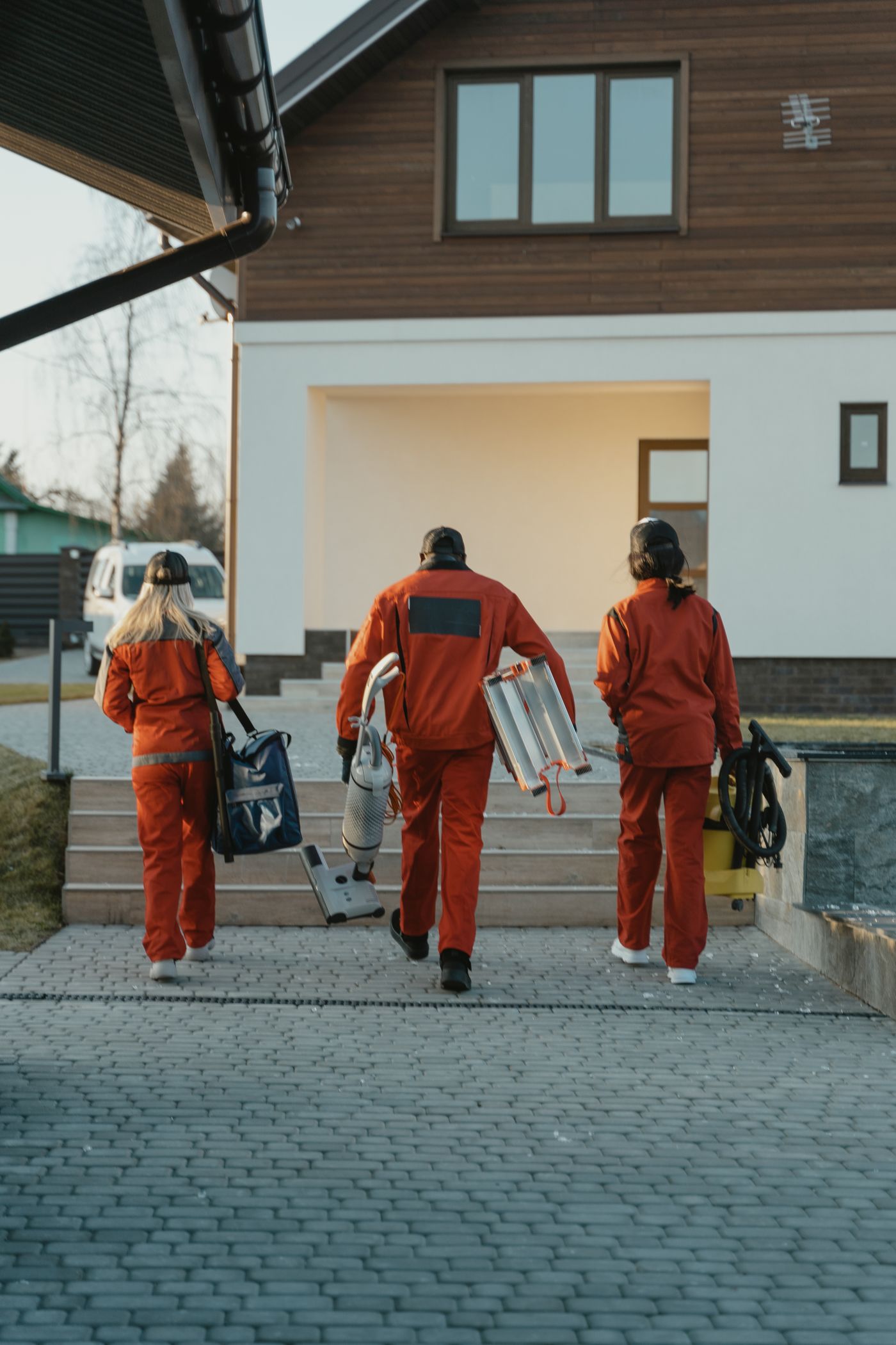 道具を持ったスタッフ3人が、依頼先の家の玄関に向かって歩いているところ