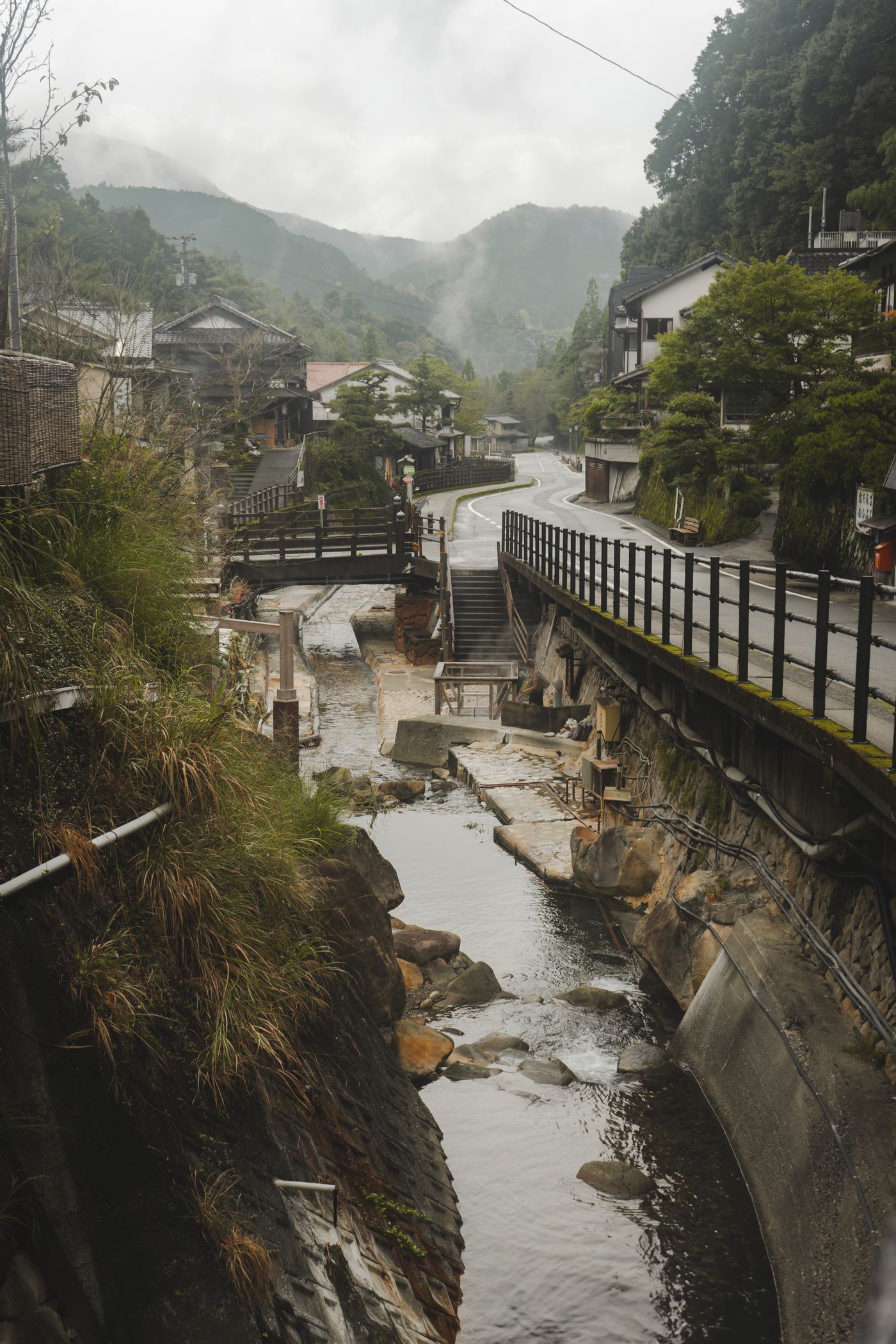 山あいの温泉地。川沿いに宿が並び、湯気が立ちのぼっている