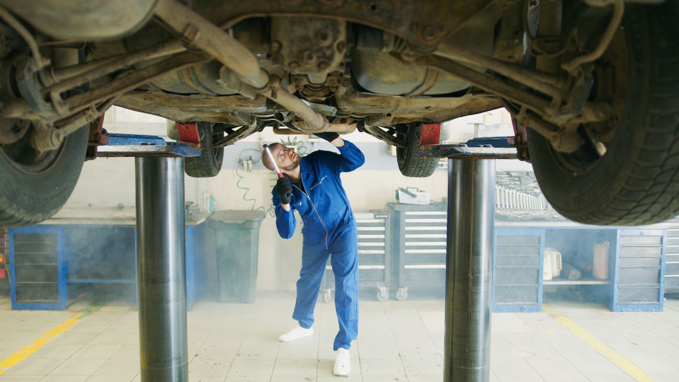 2柱リフトで持ち上げた車の下回りを、ライトを当てて点検している整備士