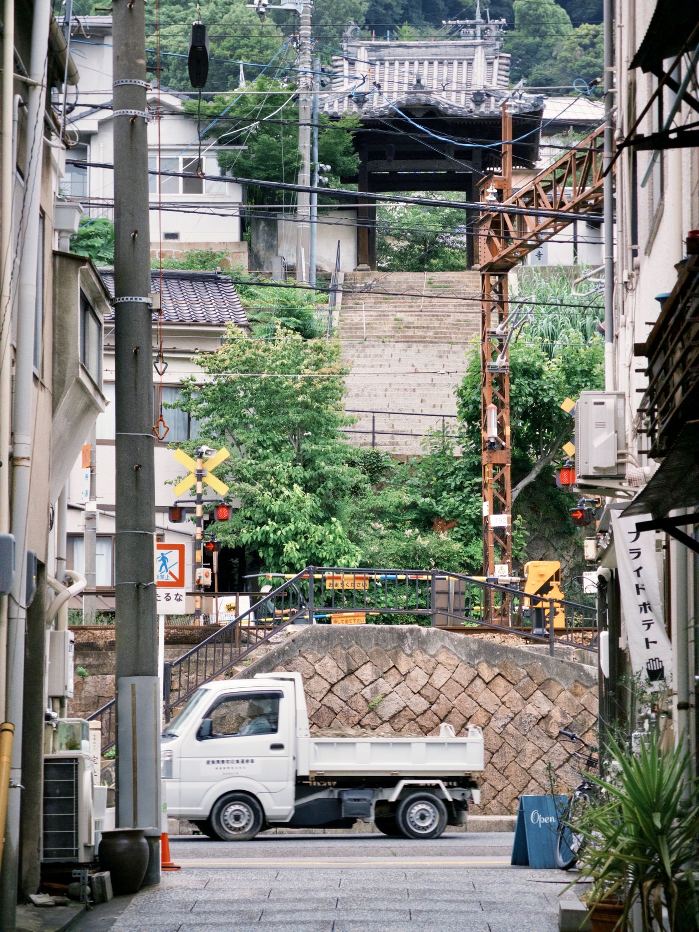住宅と電柱が並ぶ坂道の下に、小型トラックが一台停まっている町の風景